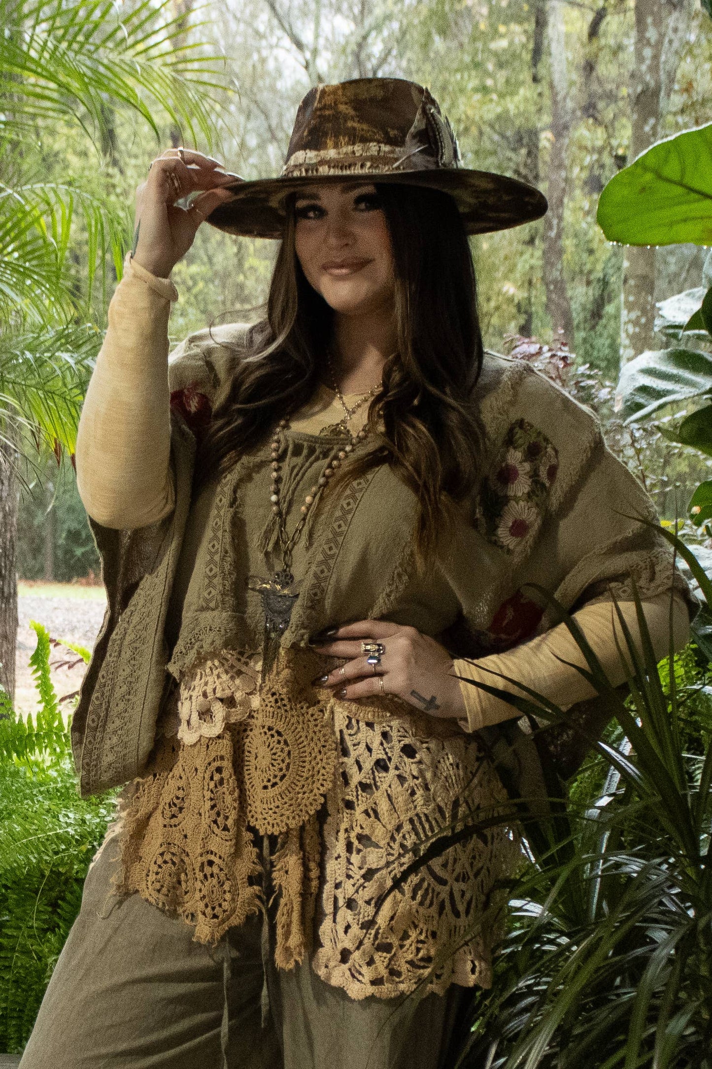 Woman in a forest setting wearing a wide-brimmed hat and patterned outfit.