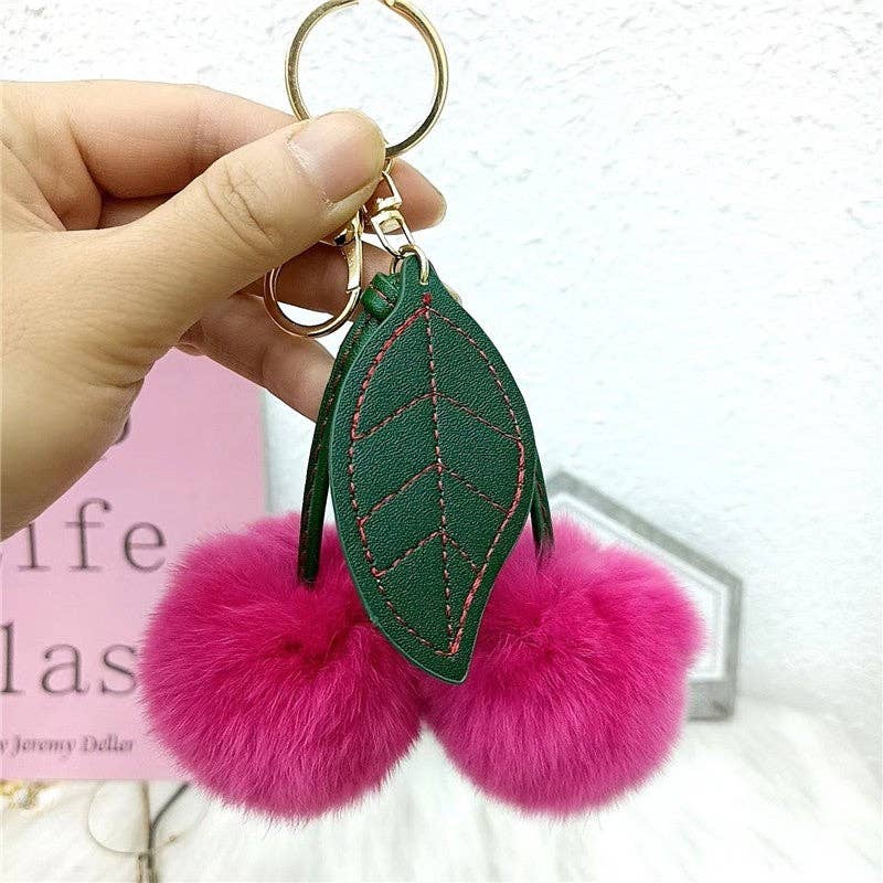 A fluffy cherry rex rabbit fur keychain with two red pompoms shaped like cherries attached to a green leaf pendant.