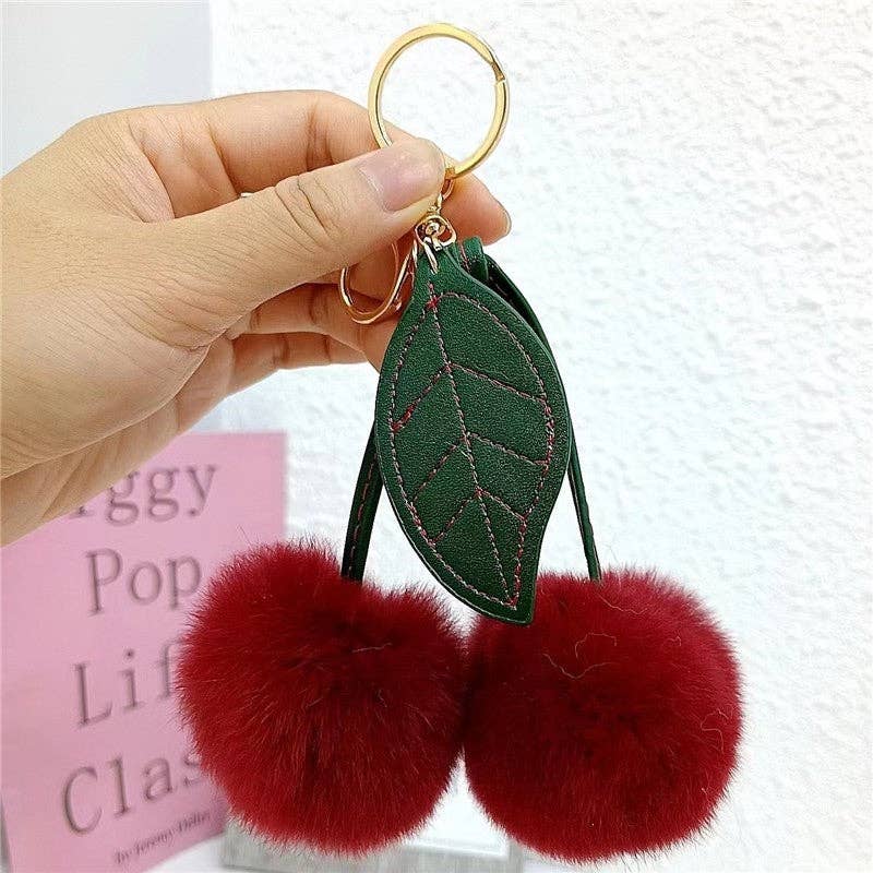 A fluffy cherry rex rabbit fur keychain with two red pompoms shaped like cherries attached to a green leaf pendant.